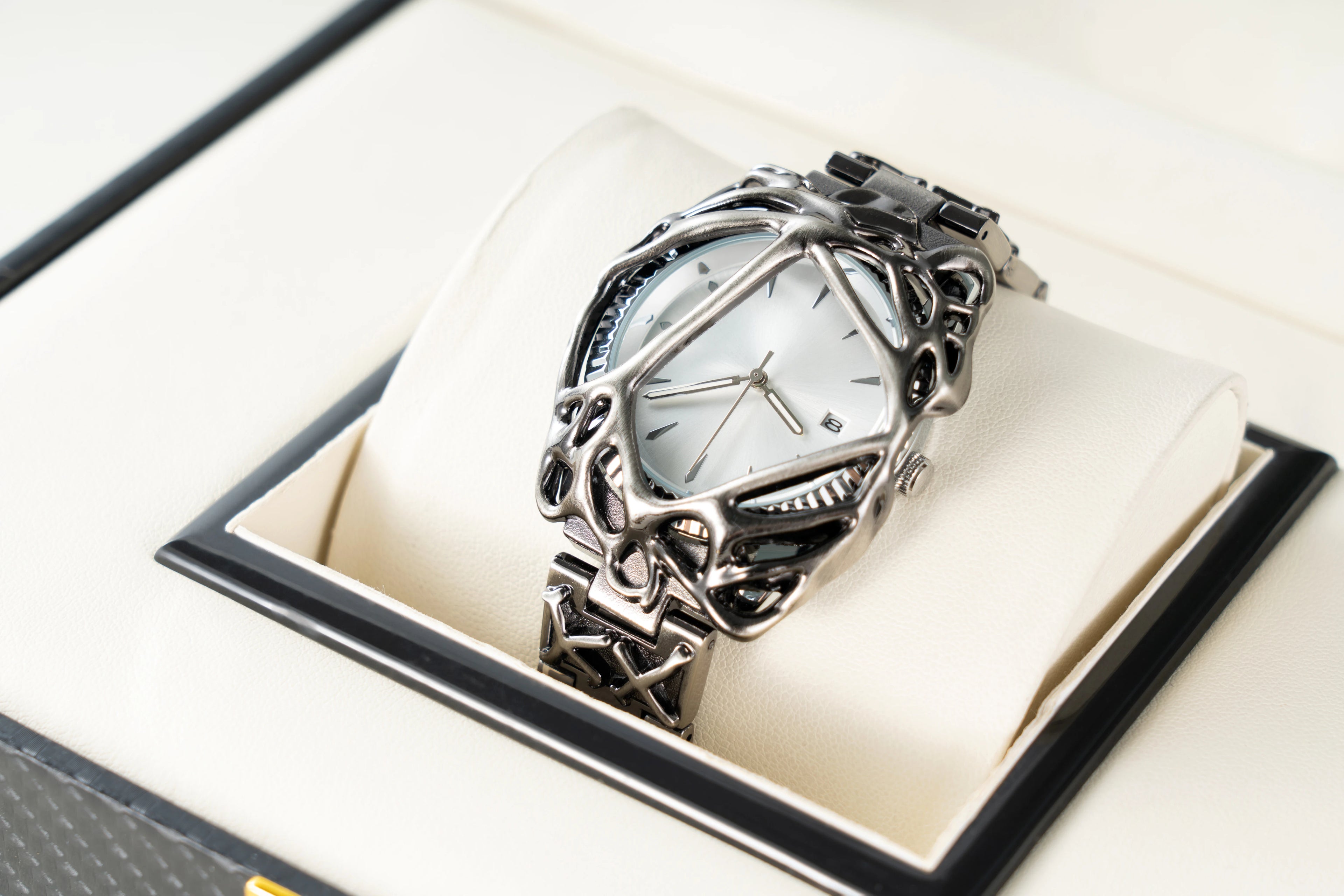 Modern silver wristwatch with intricate metal frame and leather strap displayed on cream cushion