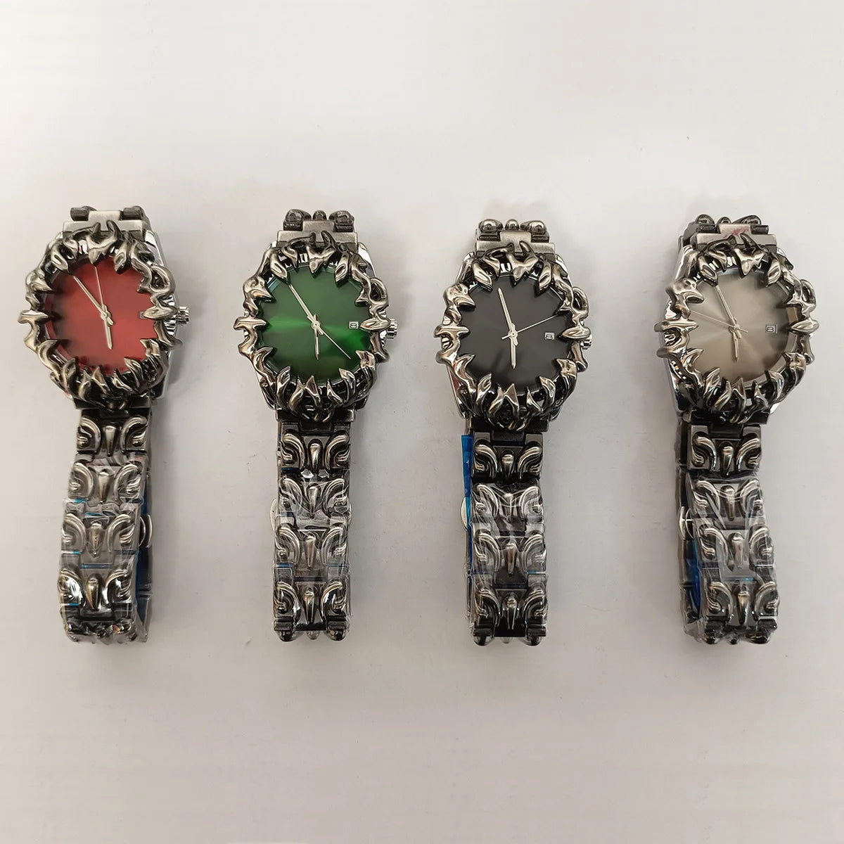 Four ornate silver wristwatches with textured bands and flame-like bezels in red, green, gray, and beige faces